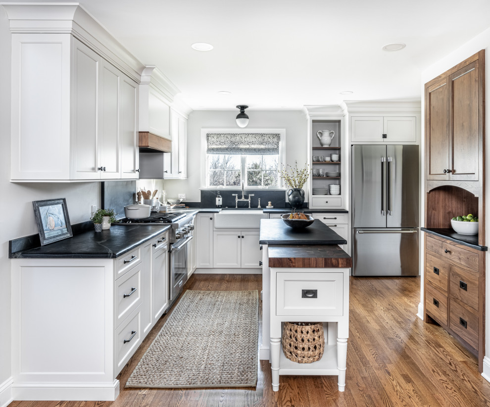 Mid-sized transitional l-shaped medium tone wood floor and brown floor eat-in kitchen photo in Philadelphia with a farmhouse sink, shaker cabinets, gray cabinets, soapstone countertops, black backsplash, stone slab backsplash, stainless steel appliances, an island and black countertops