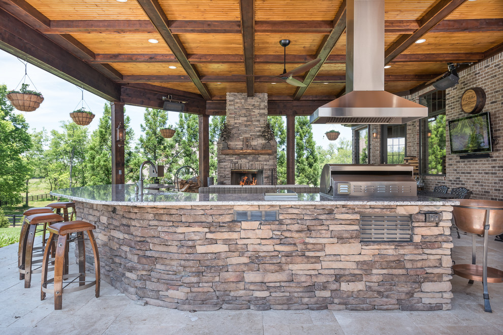 Example of a mountain style backyard stone patio kitchen design with a roof extension
