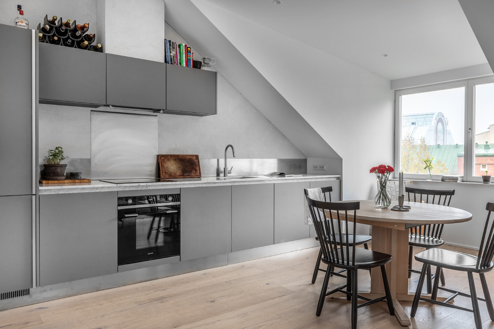 Inspiration for a scandinavian single-wall eat-in kitchen in Stockholm with an undermount sink, flat-panel cabinets, grey cabinets, marble benchtops, metallic splashback, black appliances, light hardwood floors, no island and white benchtop.
