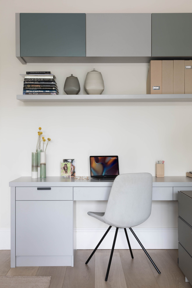 Photo of a mid-sized contemporary study room in London with white walls, a built-in desk and beige floor.