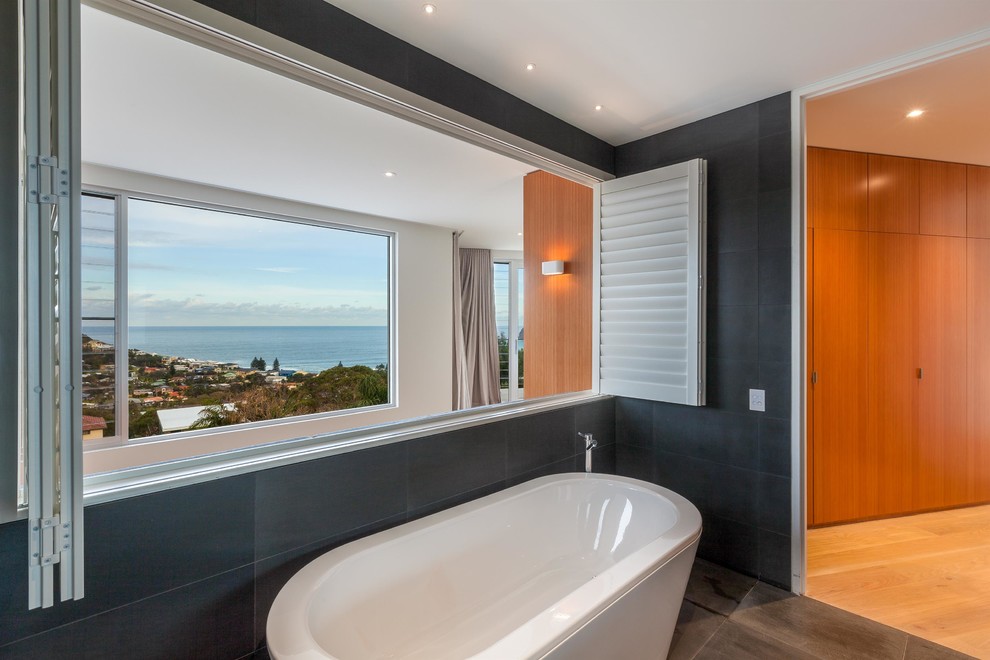 This is an example of a mid-sized contemporary master bathroom in Central Coast with flat-panel cabinets, white cabinets, a freestanding tub, gray tile, ceramic tile, ceramic floors, an integrated sink, granite benchtops, grey floor and a hinged shower door.