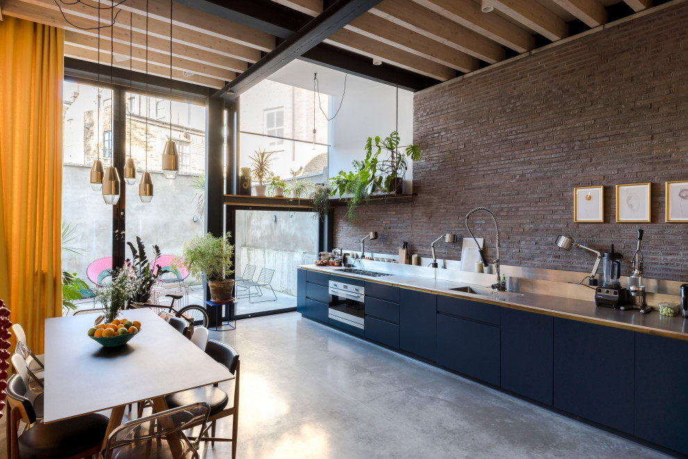Contemporary single-wall kitchen in London with an integrated sink, flat-panel cabinets, black cabinets, stainless steel benchtops, red splashback, brick splashback, stainless steel appliances, concrete floors, no island, grey floor and exposed beam.