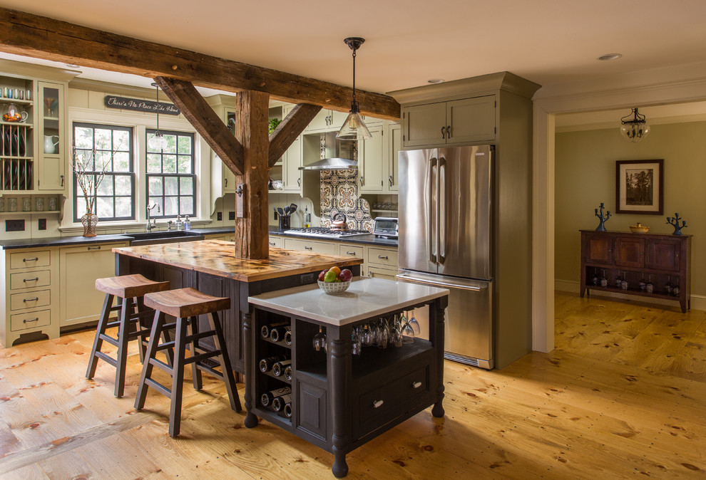 Large country l-shaped kitchen pantry in Boston with a farmhouse sink, beaded inset cabinets, green cabinets, soapstone benchtops, brown splashback, ceramic splashback, stainless steel appliances, light hardwood floors and with island.