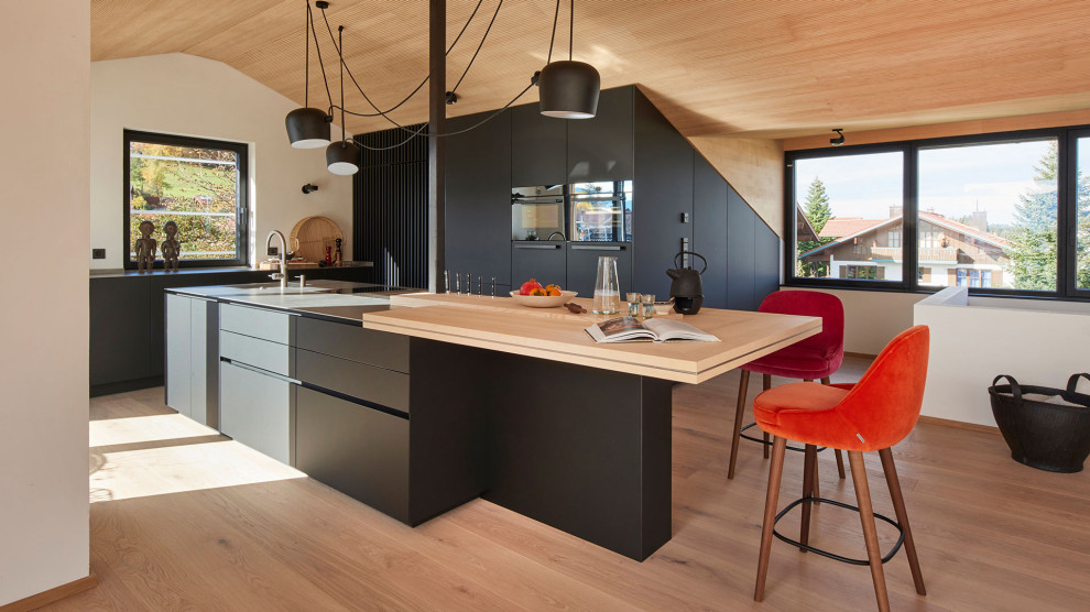 Inredning av ett modernt kök med öppen planlösning, med bänkskiva i rostfritt stål, en köksö, svarta skåp och rostfria vitvaror