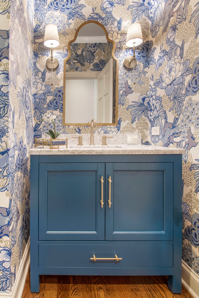 This is an example of a small transitional powder room in Chicago with shaker cabinets, blue cabinets, blue walls, medium hardwood floors, an undermount sink, engineered quartz benchtops, brown floor and white benchtops.