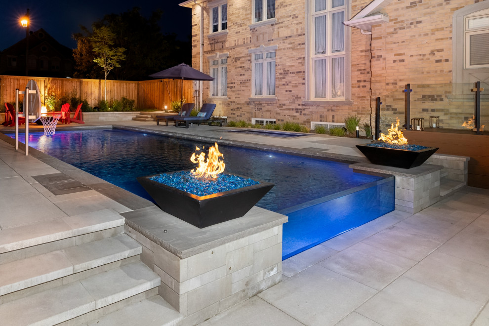 Example of a mid-sized transitional backyard concrete paver and rectangular infinity pool landscaping design in Toronto