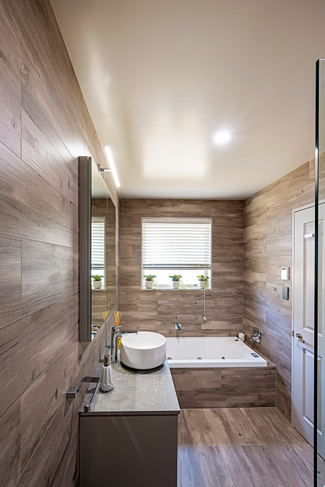 Inredning av ett medelhavsstil litet grå grått badrum, med släta luckor, bruna skåp, ett platsbyggt badkar, en öppen dusch, en toalettstol med hel cisternkåpa, brun kakel, keramikplattor, bruna väggar, klinkergolv i porslin, ett fristående handfat, bänkskiva i akrylsten, brunt golv och med dusch som är öppen
