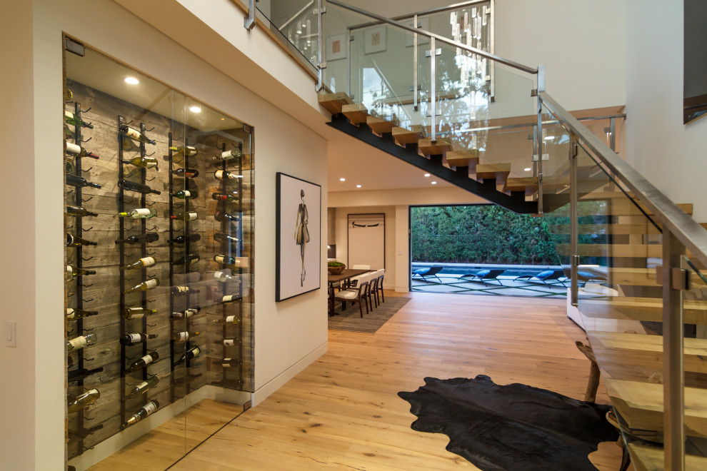 Photo of a mid-sized modern wine cellar in Los Angeles with light hardwood floors, display racks and beige floor.