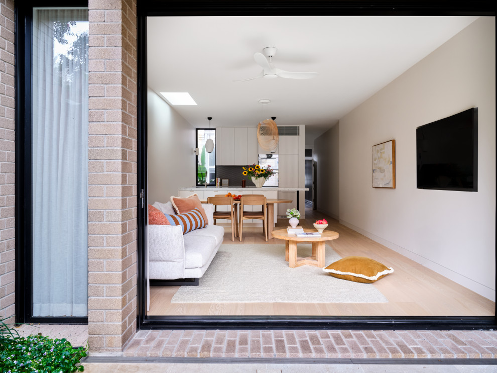 Mid-sized contemporary open concept living room in Sydney with white walls, light hardwood floors, a wall-mounted tv and brown floor.