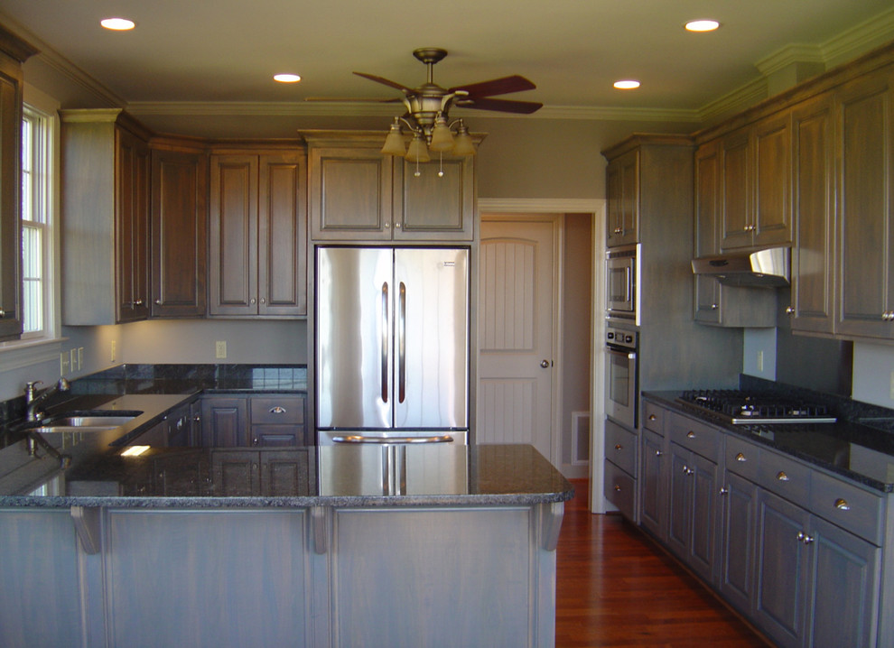 Example of a large mountain style u-shaped dark wood floor enclosed kitchen design with an undermount sink, raised-panel cabinets, medium tone wood cabinets, granite countertops, stainless steel appliances and an island
