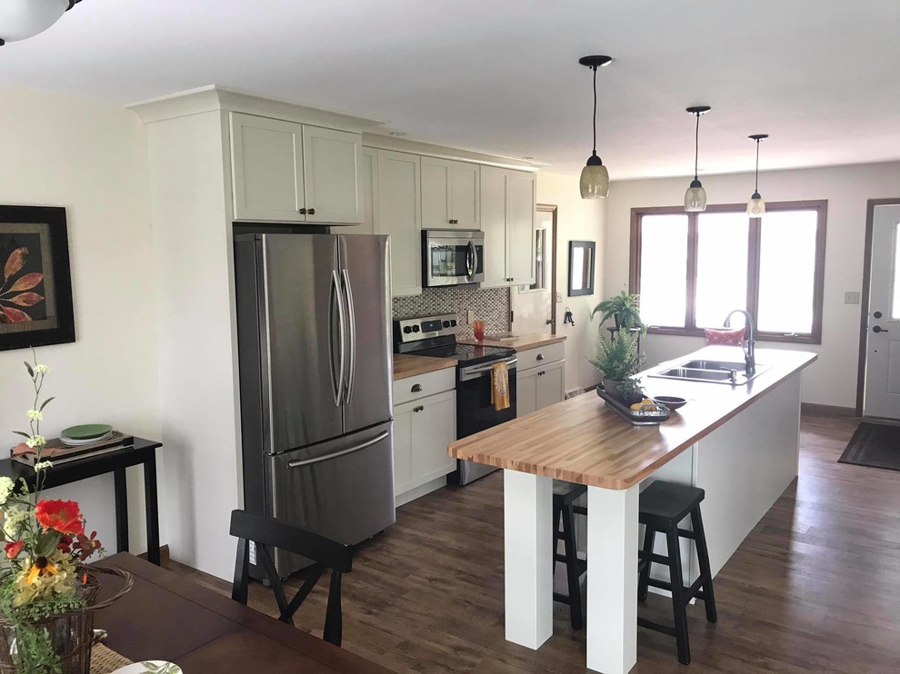 Open concept kitchen - mid-sized transitional single-wall vinyl floor and brown floor open concept kitchen idea with a drop-in sink, recessed-panel cabinets, white cabinets, wood countertops, gray backsplash, glass tile backsplash, stainless steel appliances, an island and brown countertops