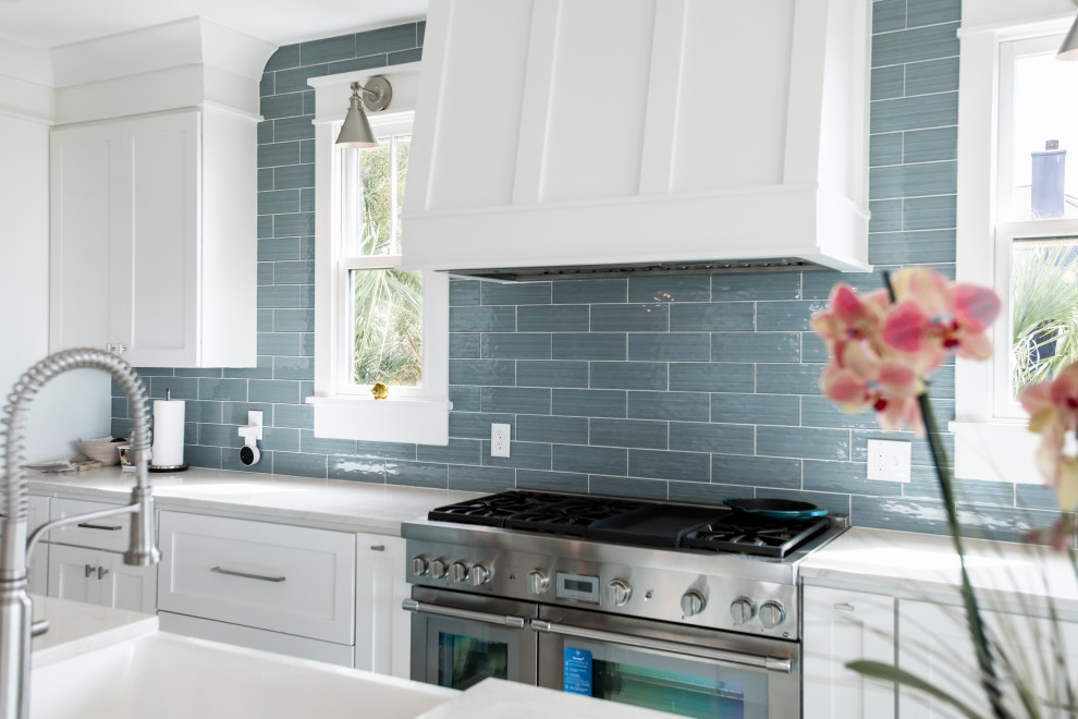 Inspiration for a large coastal l-shaped kitchen/diner in Charleston with a belfast sink, shaker cabinets, white cabinets, blue splashback, stainless steel appliances, medium hardwood flooring, an island and white worktops.