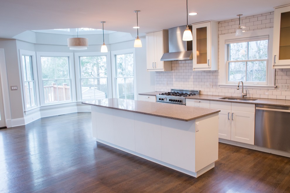 This is an example of a mid-sized transitional l-shaped open plan kitchen in New York with an undermount sink, shaker cabinets, white cabinets, granite benchtops, white splashback, subway tile splashback, stainless steel appliances, dark hardwood floors and with island.