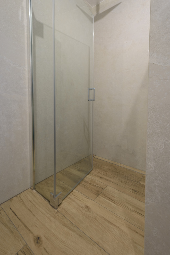 Modern inredning av ett badrum, med släta luckor, vita skåp, en kantlös dusch, grå kakel och brunt golv