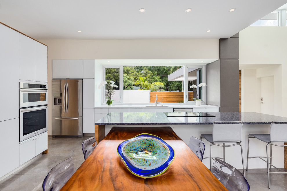 This is an example of a tropical l-shaped kitchen in Tampa with flat-panel cabinets, white cabinets, quartz benchtops, stainless steel appliances and concrete floors.