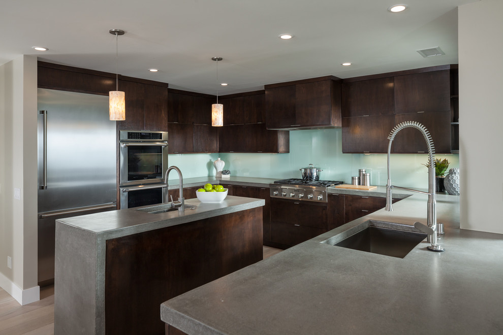 This is an example of a large contemporary u-shaped eat-in kitchen in Orange County with a drop-in sink, dark wood cabinets, concrete benchtops, blue splashback, glass tile splashback, stainless steel appliances, with island, flat-panel cabinets and porcelain floors.