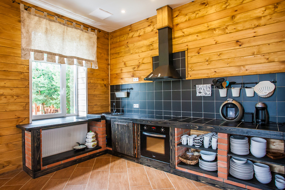 This is an example of a country l-shaped kitchen in Saint Petersburg with a single-bowl sink, open cabinets, dark wood cabinets, tile benchtops, black splashback, black appliances, no island and brown floor.