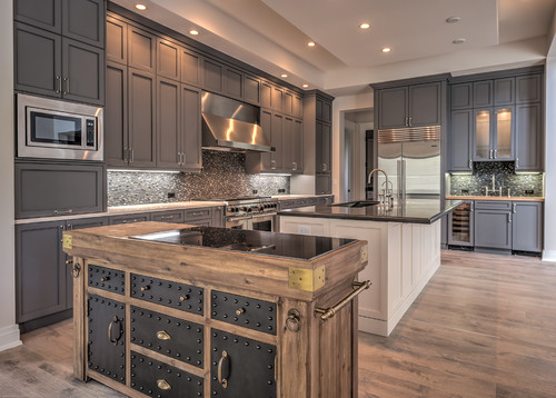 Luxury chef’s kitchen with tall gray shaker kitchen cabinet doors, mosaic tile backsplash, double islands (one rustic wood), and stainless steel appliances under recessed lighting.