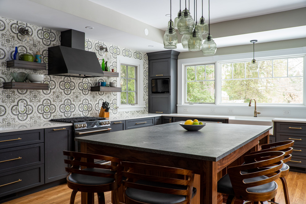 Photo of a large transitional l-shaped eat-in kitchen in Baltimore with a farmhouse sink, shaker cabinets, grey cabinets, soapstone benchtops, multi-coloured splashback, cement tile splashback, black appliances, medium hardwood floors, with island, brown floor, grey benchtop and recessed.