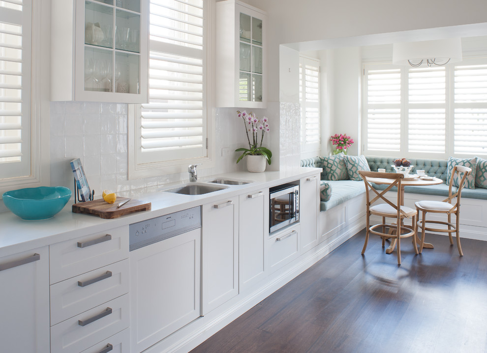 Inspiration for a mid-sized transitional l-shaped eat-in kitchen in Sydney with an undermount sink, shaker cabinets, white cabinets, quartz benchtops, white splashback, porcelain splashback, stainless steel appliances, dark hardwood floors, no island and brown floor.