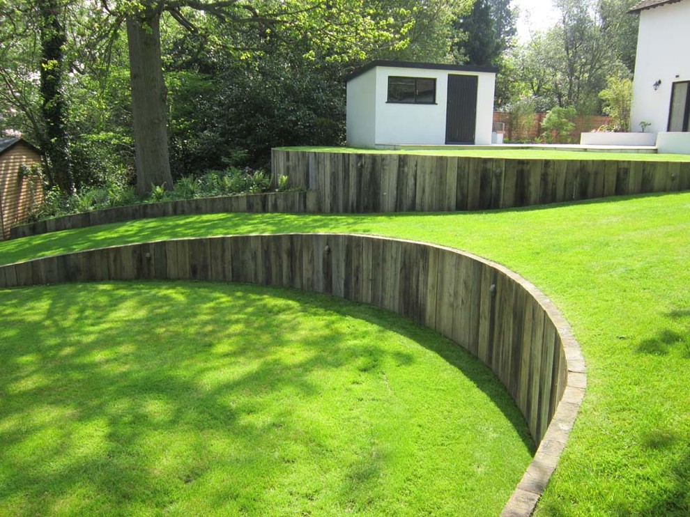 Immagine di un grande giardino formale moderno con un muro di contenimento, un pendio, una collina o una riva e pavimentazioni in pietra naturale