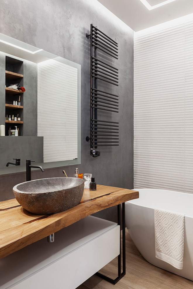 This is an example of a contemporary bathroom in Moscow with flat-panel cabinets, white cabinets, a freestanding tub, white tile, grey walls, light hardwood floors, a vessel sink, wood benchtops, beige floor and brown benchtops.
