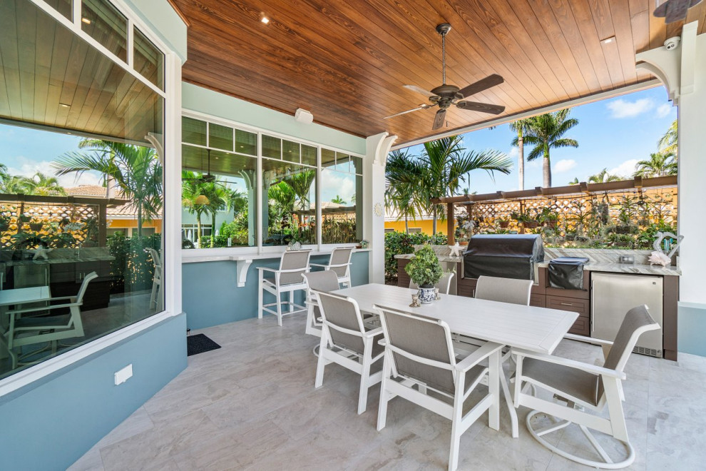 Large coastal back patio in Miami with an outdoor kitchen, tiled flooring and a roof extension.
