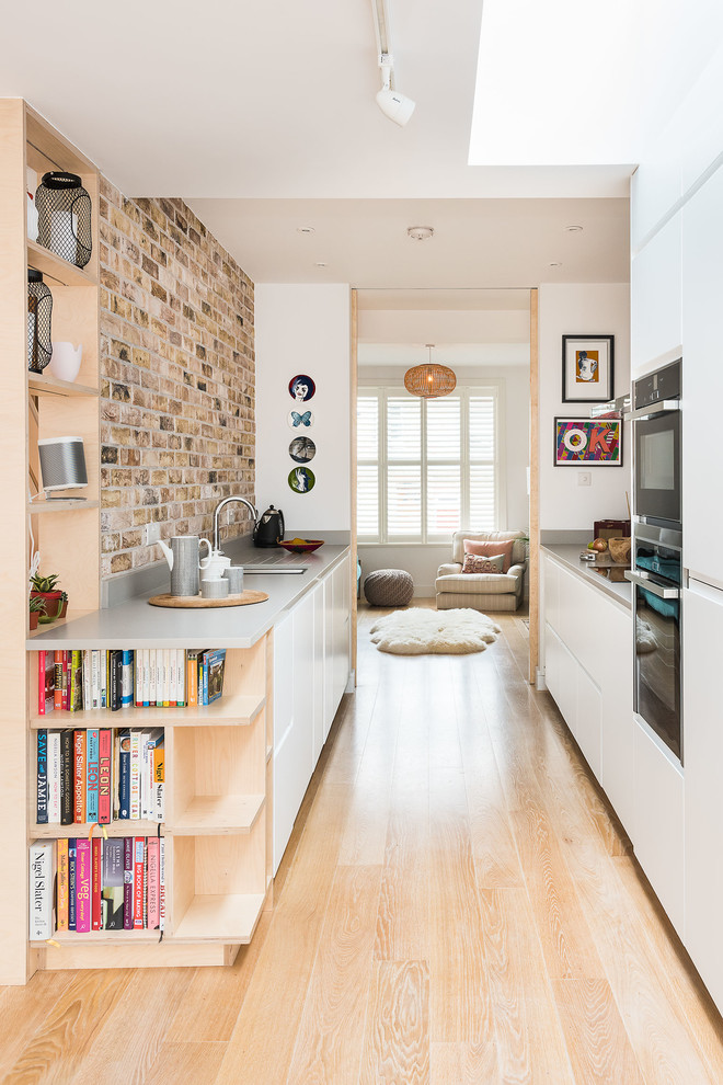 Photo of a mid-sized scandinavian galley kitchen in London with flat-panel cabinets, brick splashback, bamboo floors and beige floor.