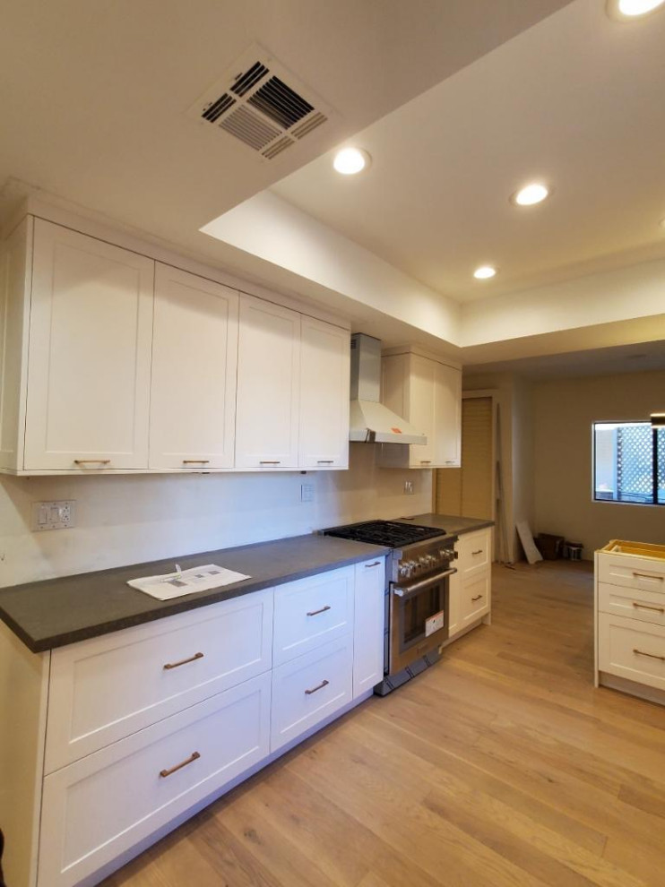 Mid-sized contemporary galley eat-in kitchen in Los Angeles with a double-bowl sink, shaker cabinets, white cabinets, quartz benchtops, ceramic splashback, stainless steel appliances, light hardwood floors, a peninsula and grey benchtop.