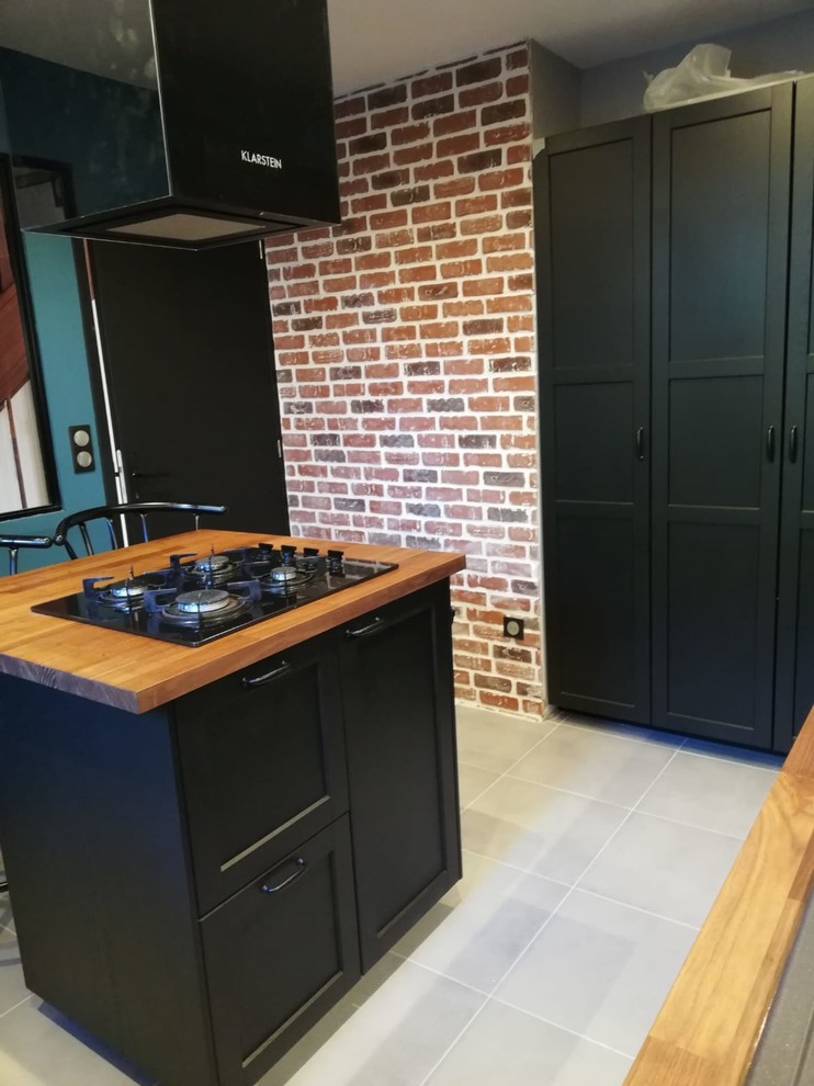 Photo of a mid-sized industrial l-shaped separate kitchen in Paris with a double-bowl sink, flat-panel cabinets, black cabinets, wood benchtops, grey splashback, slate splashback, stainless steel appliances, ceramic floors, with island, grey floor and brown benchtop.