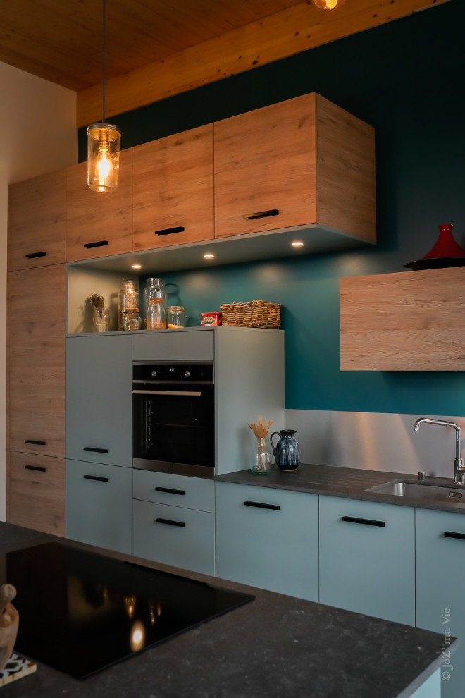 Photo of a mid-sized modern galley open plan kitchen in Lyon with an integrated sink, blue cabinets, metallic splashback, stainless steel appliances, ceramic floors, with island, blue floor, grey benchtop and exposed beam.