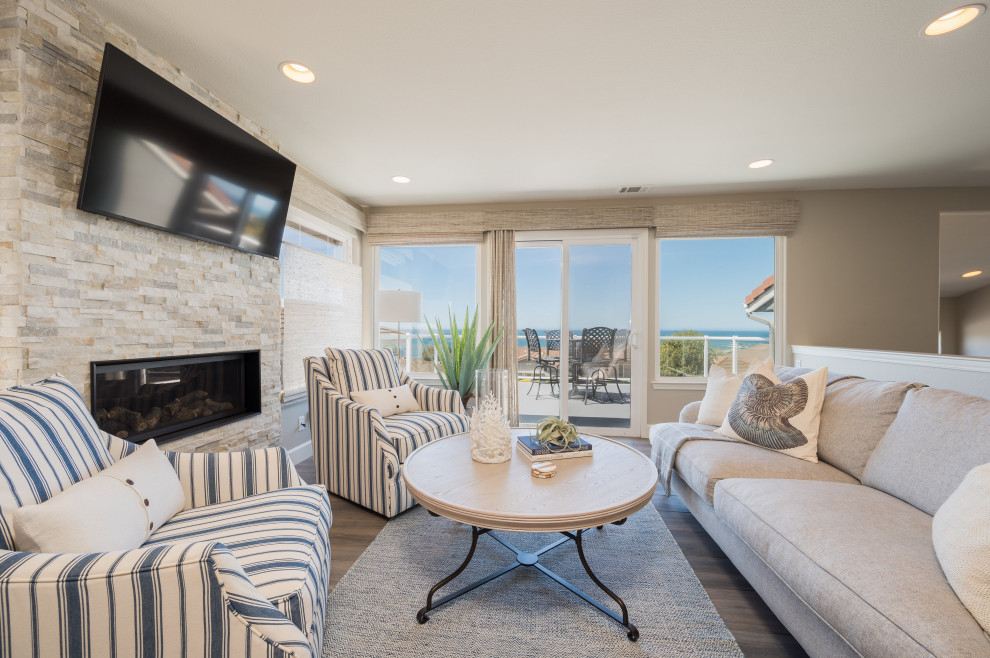 This is an example of a mid-sized beach style open concept family room in San Luis Obispo with beige walls, laminate floors, a standard fireplace, a wall-mounted tv and brown floor.