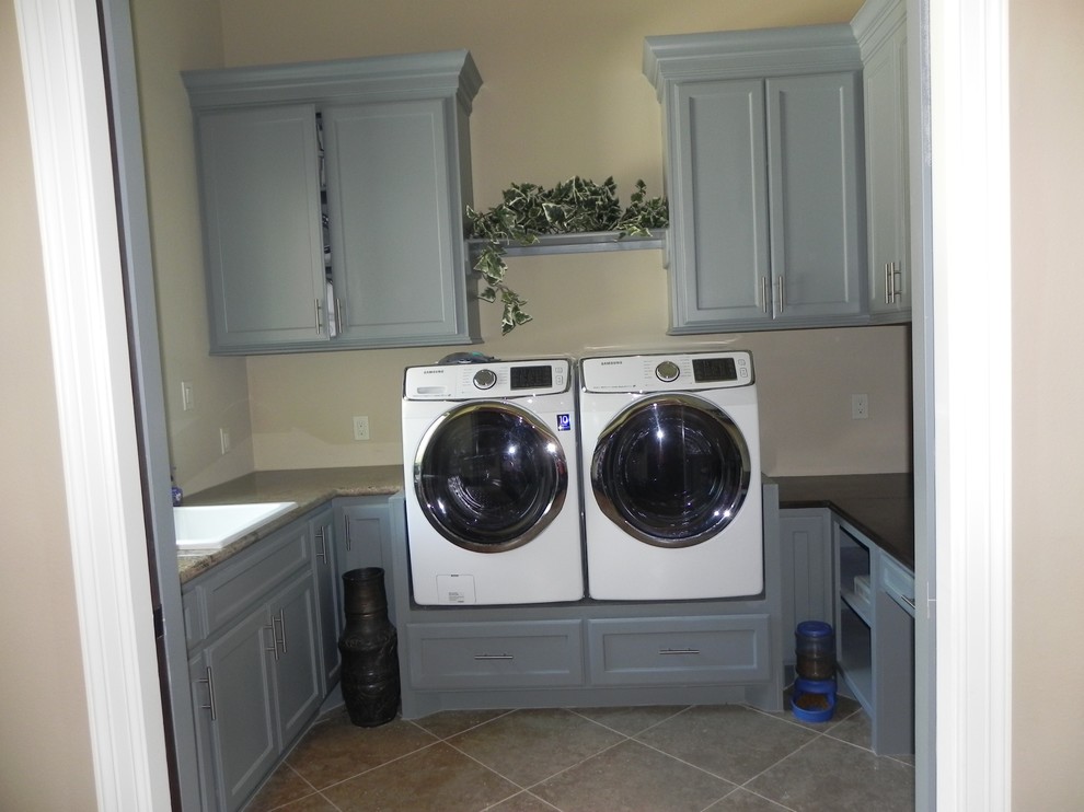 This is an example of a mediterranean dedicated laundry room in Houston with a drop-in sink, grey cabinets, granite benchtops, beige walls, porcelain floors and a side-by-side washer and dryer.
