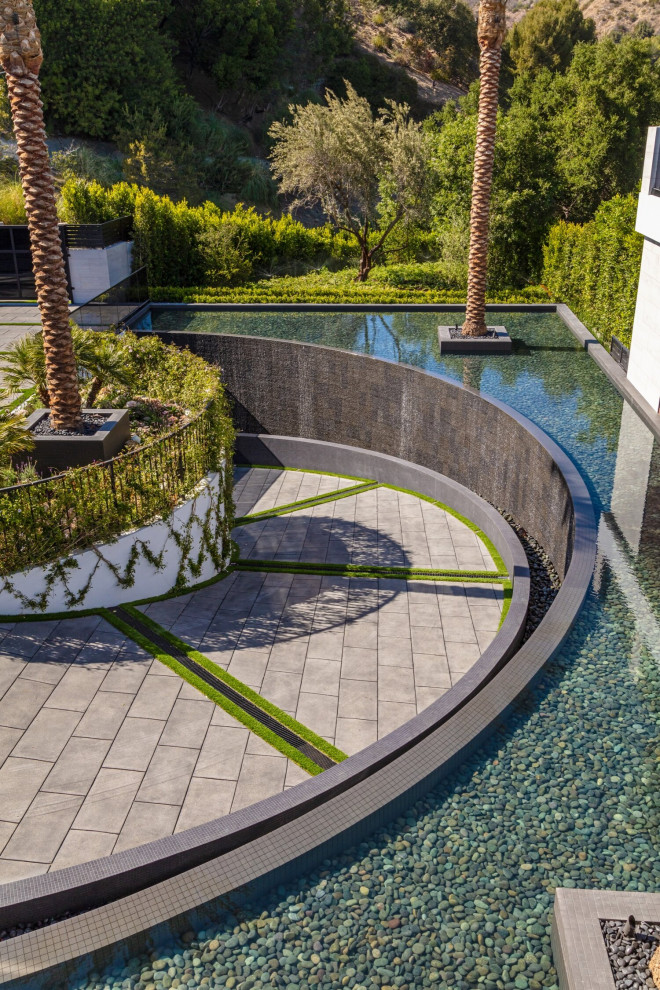 Photo of a large modern front yard full sun driveway in Los Angeles with with pond and a stone fence.
