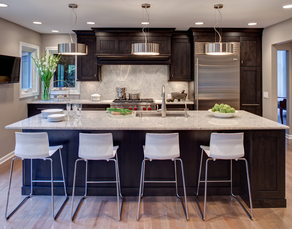 Contemporary galley kitchen in Chicago with stainless steel appliances, an undermount sink, recessed-panel cabinets, dark wood cabinets, white splashback and stone slab splashback.