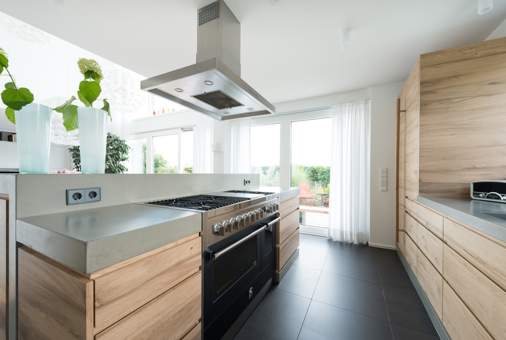Photo of a mid-sized contemporary single-wall open plan kitchen in Other with a single-bowl sink, flat-panel cabinets, light wood cabinets, concrete benchtops, white splashback, black appliances, ceramic floors, with island and grey floor.