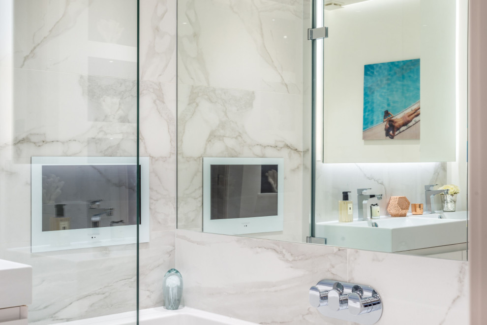 Photo of a mid-sized contemporary master bathroom in London with flat-panel cabinets, white cabinets, a drop-in tub, a shower/bathtub combo, a wall-mount toilet, blue tile, ceramic tile, grey walls, ceramic floors, a wall-mount sink, pink floor, a hinged shower door, a double vanity, a built-in vanity and recessed.
