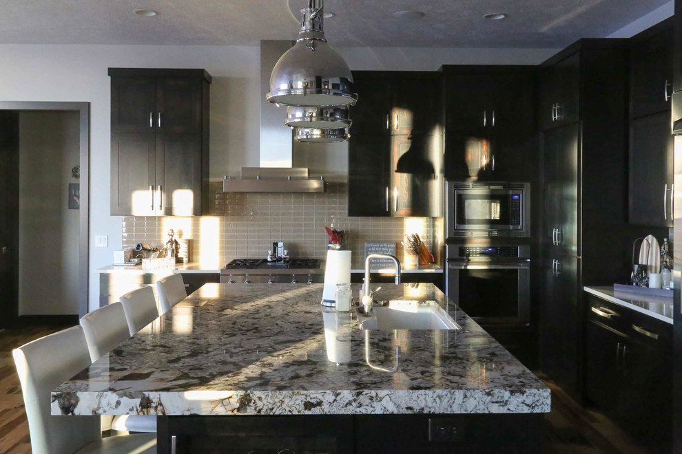 Example of a large transitional l-shaped medium tone wood floor and brown floor eat-in kitchen design with an undermount sink, shaker cabinets, black cabinets, granite countertops, beige backsplash, porcelain backsplash, stainless steel appliances, an island and multicolored countertops