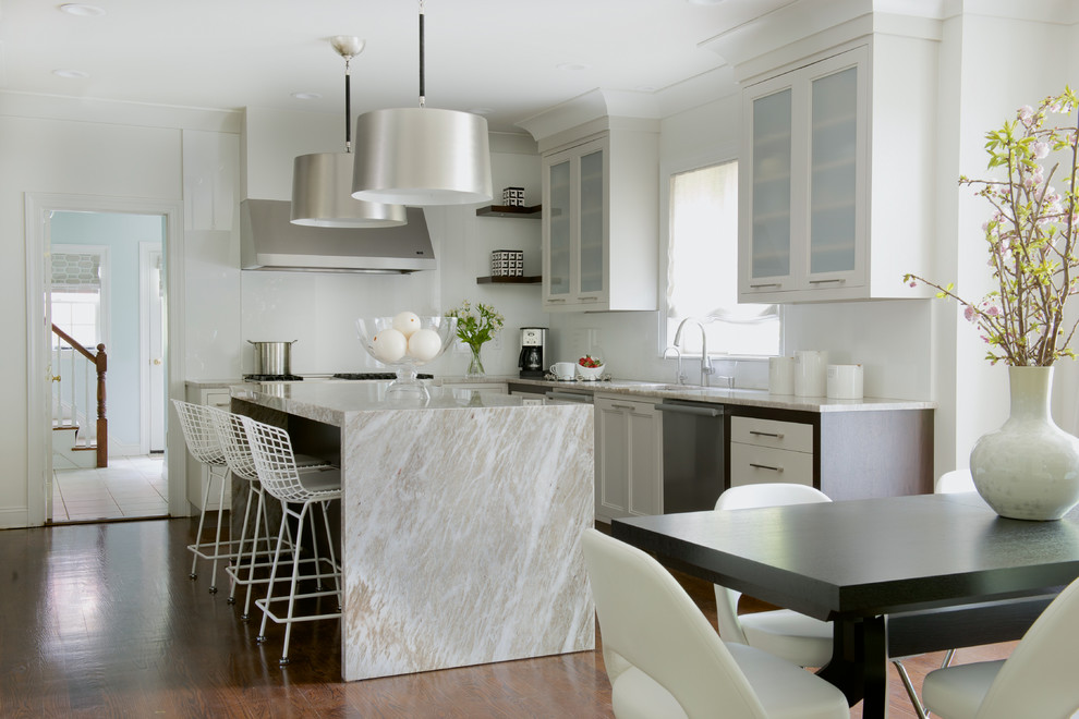 This is an example of a transitional l-shaped eat-in kitchen in New York with glass-front cabinets, white cabinets, white splashback, dark hardwood floors and with island.