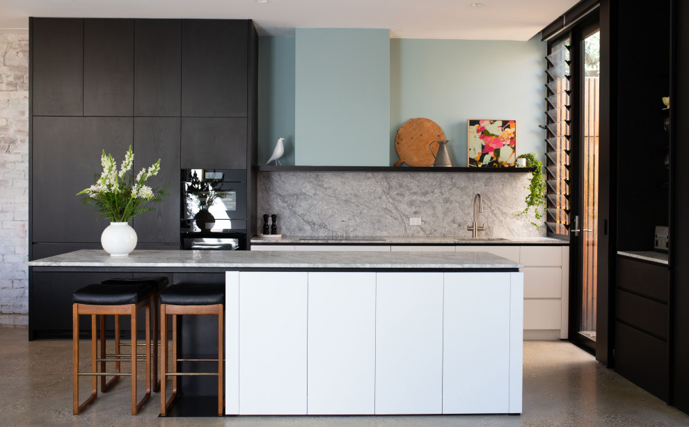 Inspiration for a medium sized grey and white open plan kitchen in Melbourne with a submerged sink, white cabinets, marble worktops, grey splashback, marble splashback, black appliances, concrete flooring, grey floors, grey worktops, an island and flat-panel cabinets.