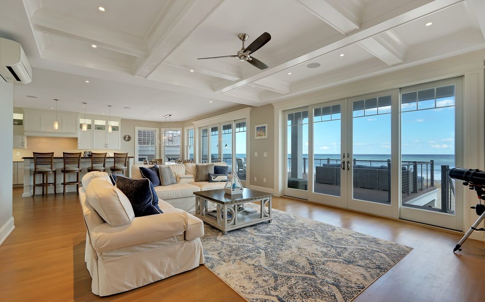 This is an example of a large beach style open concept living room in New York with beige walls, light hardwood floors, a standard fireplace, a tile fireplace surround, a wall-mounted tv and beige floor.