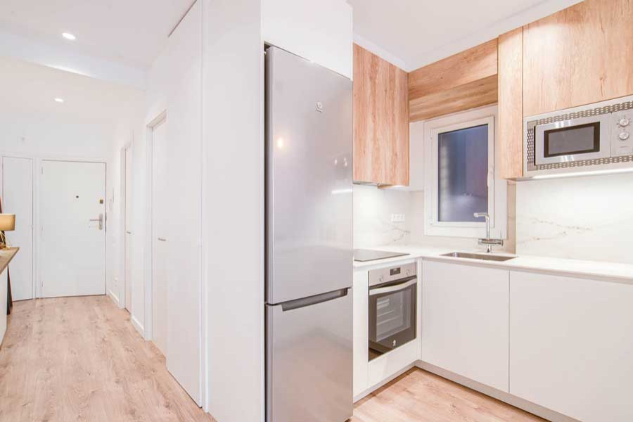 Photo of a small scandinavian single-wall laundry cupboard in Barcelona with an undermount sink, flat-panel cabinets, white cabinets, quartz benchtops, white splashback, marble splashback, white walls, medium hardwood floors, a stacked washer and dryer, brown floor and white benchtop.