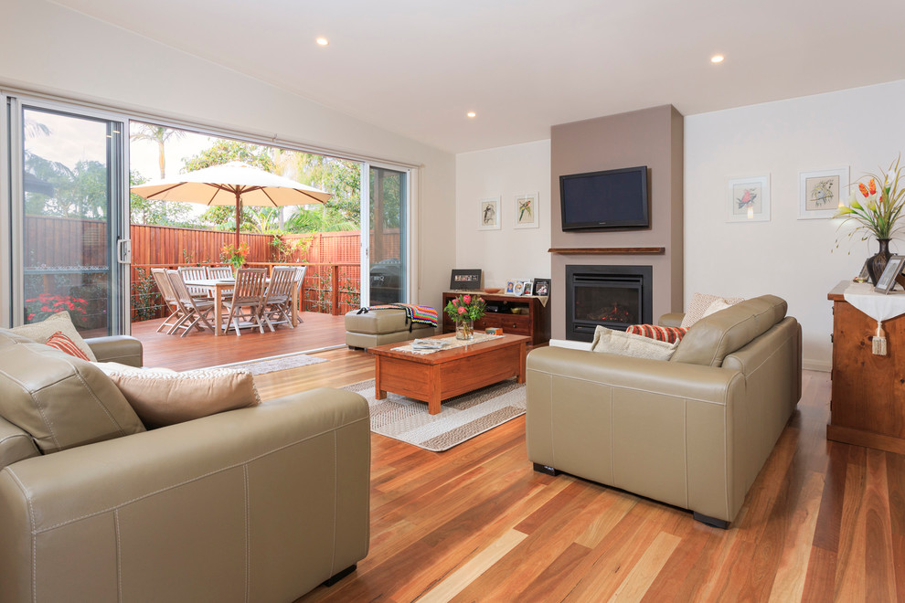 Inspiration for a mid-sized contemporary open concept living room in Central Coast with beige walls, light hardwood floors, a standard fireplace, a metal fireplace surround and a wall-mounted tv.