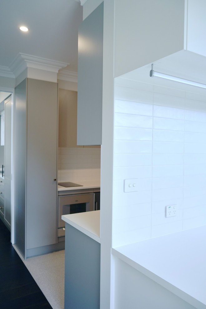 Inspiration for a mid-sized transitional single-wall dedicated laundry room in Sydney with a drop-in sink, flat-panel cabinets, white cabinets, laminate benchtops, white splashback, subway tile splashback, white walls, concrete floors, a side-by-side washer and dryer, grey floor and white benchtop.