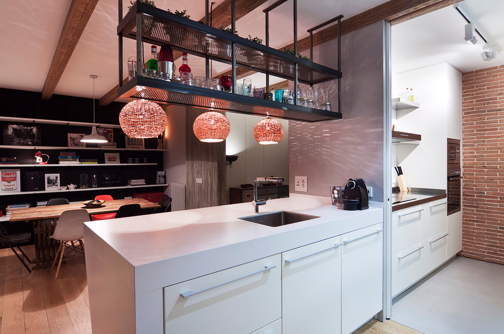 Mid-sized contemporary single-wall eat-in kitchen in Madrid with an undermount sink, flat-panel cabinets, white cabinets, white splashback, stainless steel appliances, light hardwood floors and a peninsula.