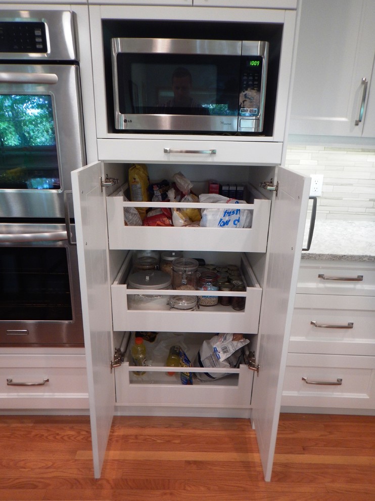 Example of a large transitional l-shaped light wood floor eat-in kitchen design with an undermount sink, recessed-panel cabinets, white cabinets, quartz countertops, gray backsplash, stone tile backsplash, stainless steel appliances and an island