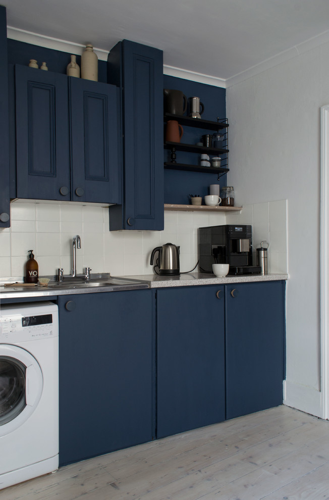 Design ideas for a mid-sized scandinavian separate kitchen in Kent with a drop-in sink, flat-panel cabinets, blue cabinets, laminate benchtops, white splashback, cement tile splashback, stainless steel appliances, light hardwood floors, no island, white floor and multi-coloured benchtop.