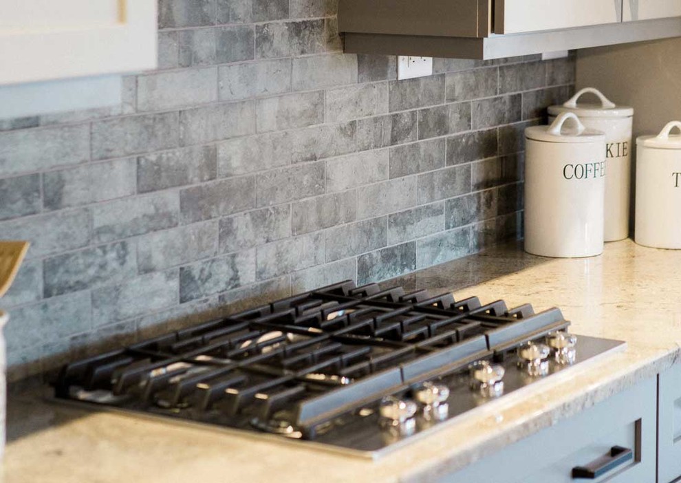 Mid-sized transitional kitchen photo with a farmhouse sink, granite countertops, gray backsplash, stainless steel appliances and an island