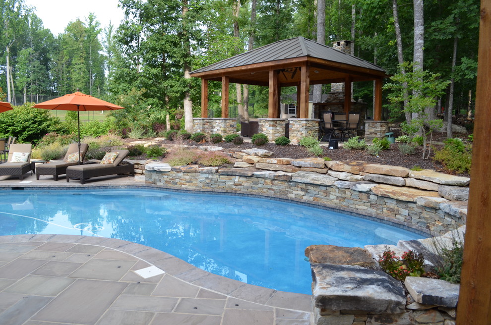 This is an example of a mid-sized country backyard custom-shaped pool in DC Metro with natural stone pavers.