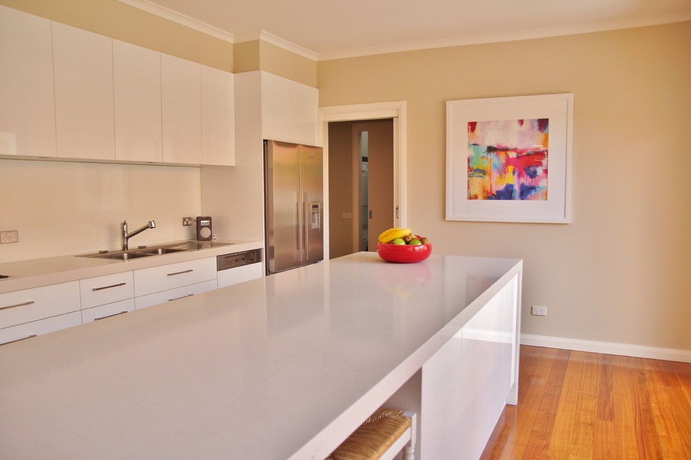 Mid-sized contemporary galley eat-in kitchen in Melbourne with a double-bowl sink, flat-panel cabinets, white cabinets, quartz benchtops, white splashback, glass sheet splashback, stainless steel appliances, medium hardwood floors and with island.